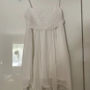 Vit axelbandsklänning med plisserad överdel - Söt vit klänning med tunna axelband och plisserad överdel. Kjolen är luftig och faller fint, perfekt för varma dagar. Smockad rygg för extra komfort och passform. Stilren och enkel design som passar till många tillfällen. Skriv om fler bilder eller frågor! Kan gå ner i pris💕💕