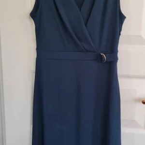 Marinblå omlottklänning från H&M - Säljer en marinblå ärmlös klänning från H&M i omlottmodell med bälte i midjan. Klänningen har en v-ringad överdel och är tillverkad i ett mjukt, lätt material som ger en snygg siluett. Perfekt för dig som gillar stilrena och klassiska plagg.