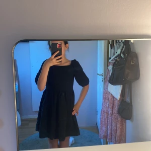 Svart kortklänning med puffärm från Kappahl - Säljer en svart kortklänning från Kappahl med puffiga kortärmar och markerad midja. Klänningen har en lätt strukturerad yta och rund halsringning. Perfekt för dig som gillar en klassisk och stilren look.