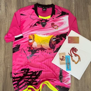 Rosa fotbollströja från 90 Minutes - Säljer en riktigt snygg rosa fotbollströja från 90 Minutes med coolt grafiskt tryck i gult, svart och vitt. Tröjan har korta ärmar, svart och gul detalj vid halsen och unika motiv framtill. Perfekt för dig som vill sticka ut på planen!