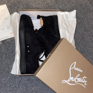 Svarta äkta loubs  - Säljer ett par svarta sneakers från Christian Louboutin i mocka med svarta nitar på tån och klassisk röd sula. Skorna har snörning och en rund tå. Perfekta för dig som vill sticka ut med exklusiva detaljer.