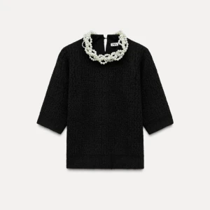 Svart stickad topp med pärldetalj från Zara - Säljer en svart stickad topp från Zara med trekvartsärm och en snygg pärlkedja runt halsen. Perfekt för dig som vill ha något extra till outfiten! Toppen har en rak passform och känns både trendig och elegant.
