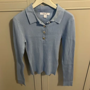 Ljusblå ribbad pikétröja från Amisu - Säljer en ljusblå långärmad pikétröja från amisu. Tröjan är ribbad och har en klassisk krage samt tre hjärtformade knappar framtill. Perfekt för en stilren och bekväm look. Aldrig använt 