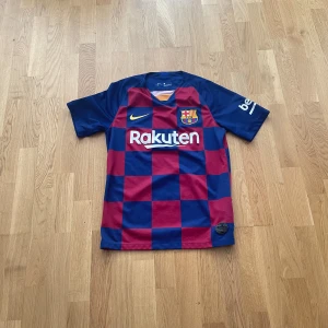 FC Barcelona hemmatröja 2019/2020 - Säljer en officiell FC Barcelona hemmatröja från säsongen 2019/2020. Tröjan är kortärmad med blå och röda rutor, Nike-logga och klubbmärke på bröstet samt La Liga-märke på ärmen. Materialet är lätt och andas, perfekt för fotbollsträning eller match.