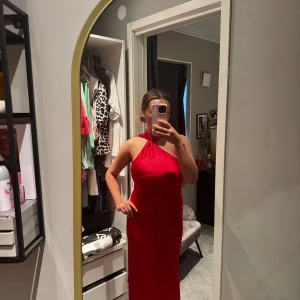 Röd långklänning med halterneck - Säljer en elegant röd långklänning med halterneck och öppen rygg. Klänningen är figurnära med ett långt band som knyts i nacken. Perfekt för speciella tillfällen som aftonklänning eller balklänning!!