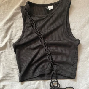 Svart ribbad topp - En svart ribbad croppad topp från H&M Divided. Toppen har snörningsdetalj framtill som går diagonalt över bröstet. 