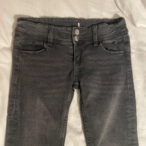Grå bootcut low waist jeans - Snygga grå bootcut jeans med låg midja och dubbla knappar fram. Jeansen har bakfickor med ficklock och knappar bak. Perfekta för en avslappnad stil.