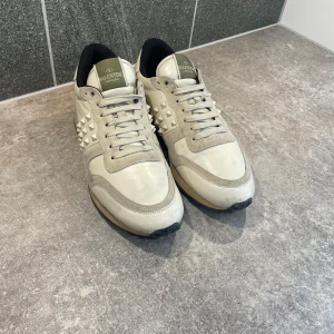 Beige sneakers från Valentino - Snygga beige sneakers från Valentino med ikoniska nitar på sidorna. Skorna har en kombination av skinn och mocka, vilket ger en lyxig känsla. Perfekta för att lyfta din stil med en touch av elegans.