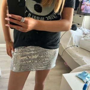 Glittrig silverkjol - Snygg och glittrig kortkjol i silver med paljetter. Perfekt för en utekväll eller fest. Kjolen har en tight passform som framhäver figuren. Ett måste för garderoben om du älskar att glittra! Midje mått rakt över 36-37 cm st 170 men skulle säga s-m