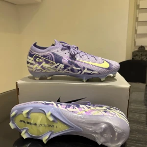 Lila fotbollsskor från Nike - Snygga lila fotbollsskor från Nike med ett iögonfallande mönster och limegröna detaljer. Skorna har snörning och är designade för optimal prestanda på planen. Perfekta för dig som vill sticka ut!