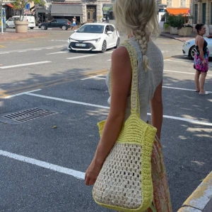 Gul och beige stickad strand väska  - Säljer en snygg stickad strand väska i gult och beige. Perfekt för en dag på stan eller stranden. Väskan har ett luftigt mönster och långa axelband för enkel bärning. Den är både praktisk och stilren, perfekt för sommarens äventyr.