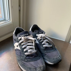 Grå sneakers från Saucony - Snygga grå sneakers från Saucony med vit snörning och detaljer i mocka. Perfekta för en avslappnad stil och bekväma att bära hela dagen. De har en klassisk design med en modern touch.