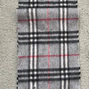 Grå rutig halsduk från Burberry - Säljer en elegant grå rutig halsduk från Burberry, tillverkad i 100% kashmir. Den har ett klassiskt rutmönster i svart, vitt och rött. Perfekt för att hålla dig varm och stilren  