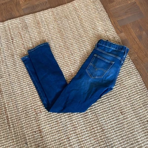 Blå jeans från Levi's - Snygga blå jeans från Levi's med klassisk femficksdesign och en bekväm passform. De har en mörk tvätt med lätt slitna detaljer och en ikonisk läderpatch baktill. Perfekta för en avslappnad stil.