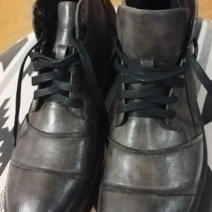 Läderkängor från "Network" med snörning - Snygga grå boots i skinn med snörning och dragkedja på sidan. De har en robust sula och en stilren design som passar perfekt för höst och vinter. Perfekta för att ge din outfit en cool touch. Läderkängor för herrar i stl. 42 från "Network". Helt nya och aldrig använda tidigare. Bra bevarade under tiden och välskötts under sin oanvända tiden, på rätt plats i sitt skåp. Säljs pga fel storlek. Mycket bekväma skor med lågt pris. 