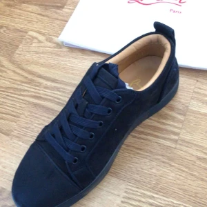 Svarta sneakers från Christian Louboutin - Snygga svarta sneakers från Christian Louboutin i mocka. Skorna har en klassisk design med snörning och en stilren look. Perfekta för dig som vill ha något exklusivt och trendigt.