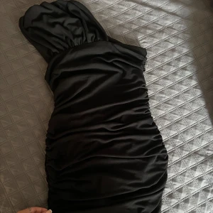 Svart axelbandslös mini- klänning - Snygg svart axelbandslös klänning med rynkade detaljer som ger en elegant look. Perfekt för en kväll ute eller en speciell tillställning. Klänningen har en tight passform som framhäver figuren. Använt cirka 1-2 gånger. 🌸