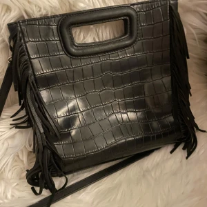 Maje väska  - Säljer nu min svarta Majeväska. Köpt på Zalando för cirka 3500 kr. Väskan är i bra skick som på bilderna. Saknar några få fransar längst ner men det syns inte. Skriv vid frågor eller för fler bilder💕💕