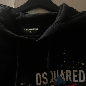 Svart hoodie från Dsquared2 - Säljer en svart/mörkblå hoodie från Dsquared2 med färgglatt tryck och texten 'ICON' på framsidan. Tröjan har en klassisk huva med dragsko och en bekväm passform. Perfekt för en avslappnad stil.