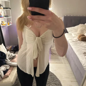 Vit knytblus - Säljer en stilren vit blus med knytning framtill. Blusen är ärmlös och har en luftig passform, perfekt för varma dagar.