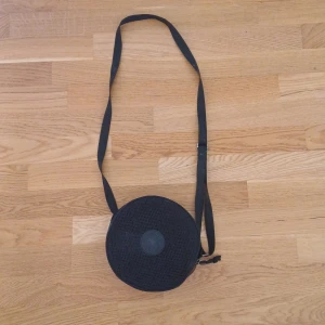 Svart rund axelväska från converse. - Snygg och praktisk svart rund axelväska med justerbar rem. Väskan har en diskret logotyp på framsidan och är perfekt för att bära med sig det nödvändigaste. Den är tillverkad i ett slitstarkt material och har en dragkedja för säker förvaring.