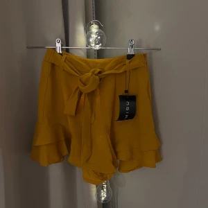 Gula shorts med volangdetaljer - Snygga gula shorts med volangdetaljer och knytband i midjan. Aldrig använt! 