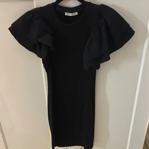 Svart klänning från Zara - Snygg svart klänning från Zara med volanger på ärmarna. Använd fåtal gånger. Går över knäna på mig, jag är 164