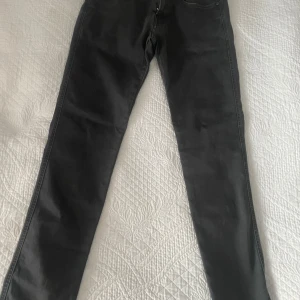 Grå Replay Anbass jeans - Säljer ett par grå-svarta Replay Hyperflex Anbass jeans i storleken 29/32. De har en modern design med fem fickor och knappgylf. Perfekta för en stilren look.