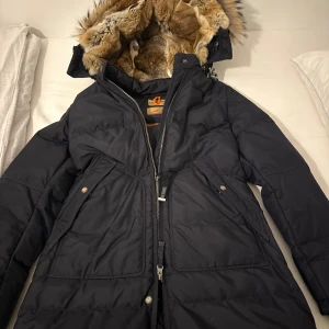 Svart dunjacka från Parajumpers - Säljer en svart dunjacka från Parajumpers med pälsfodrad huva och dragkedja. Jackan har flera praktiska fickor och en patch på ärmen. Perfekt för kalla vinterdagar. Fler bilder kan skickas om önskas. Pris kan diskuteras 