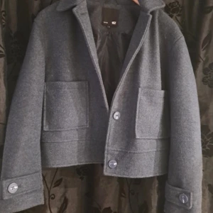 Grå ulljacka från lager 157 - Snygg grå ulljacka från lager 157, med stora fickor framtill och knappar. Jackan har en klassisk krage och är croppad i modellen. Perfekt för kyligare dagar. Lite noppig men det går att fixa med en maskin❤️