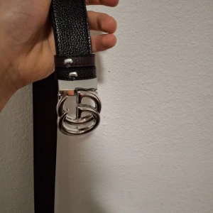 Svart och brunt bälte med utbytbara spännen - Snyggt bälte i svart och brunt med två utbytbara spännen i silver och svart. Perfekt för att variera stilen beroende på tillfälle. Bältet har en elegant design och passar till många olika outfits.