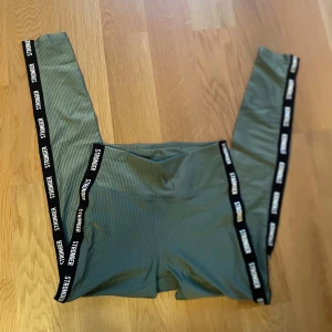 Gröna leggings från Stronger - Snygga gröna leggings från Stronger med svart resårband och vit text längs sidorna. Metallicfärg, och ribbat tyg. Perfekt för träning eller en aktiv vardag.