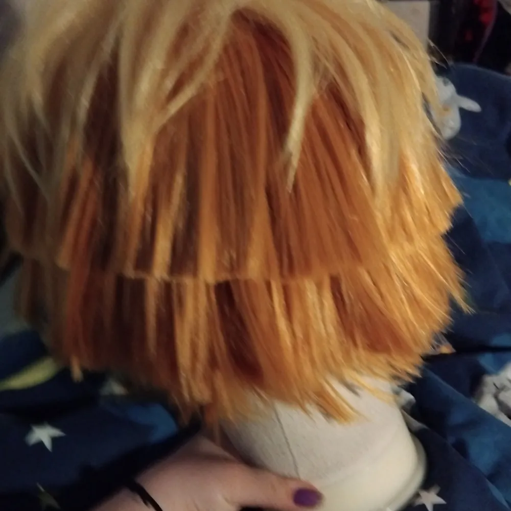 Snygg peruk i en mix av blonda och orange toner. Perfekt för cosplay eller maskerad. Den har en rufsig stil med korta längder som ger en cool look. Aldrig använd.. Asusteet.