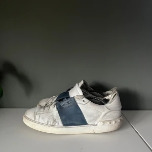 Valentino garavani sneakers i vitt och blått  - Snygga Valentino sneakers i vitt med en bred blå rem över snörningen. Skorna har en klassisk design med rund tå och platt sula. Perfekta för en stilren look. Storlek 42 men passar 43. Nya ≈ 6000kr men säljer de för 700kr. 