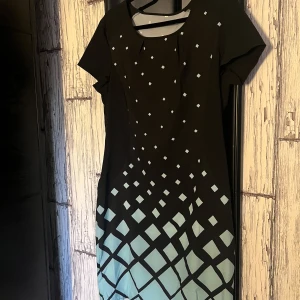 Svart och ljusblå klänning med geometriskt mönster - Snygg svart klänning med ett coolt geometriskt mönster i ljusblått. Klänningen har korta ärmar och en elegant passform som passar perfekt för olika tillfällen. Den unika designen gör den till ett blickfång i garderoben.