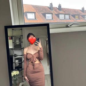 Brun offshoulder klänning - Säljer en snygg brun offshoulder klänning med lång ärm och knyt framtill. Klänningen har en tight passform och är perfekt för en kväll ute. Den är både stilren och trendig, vilket gör den till ett måste i garderoben.