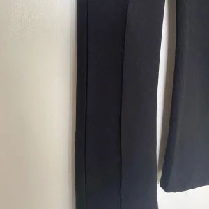 Kostymliknande byxor - Kostymliknande byxor från Gina Tricot med ett väldigt stretchiga material vilket gör dom väldigt bekväma. Utsvängda vid benen. De har en rand över benet på framsidan. Har lite skananker, en ”mask” på ena benet. Se bild. Syns inte så mycket om man inte kollar nära.