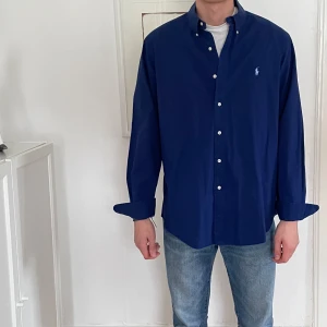 Mörkblå Ralph Lauren skjorta  - Snygg mörkblå skjorta från Ralph Lauren med klassisk krage och knappar framtill. Perfekt för en stilren look.