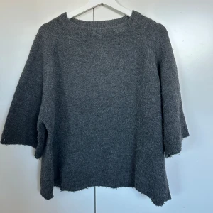 Grå stickad tröja - Mysig grå stickad tröja med en enkel design. Perfekt för kyliga dagar med sin bekväma passform och mjuka material. Tröjan har en rund hals och trekvartsärmar som ger en avslappnad look.