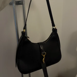 Svart axelväska med gulddetaljer - Fin svart axelväska i skinn med gulddetaljer. I mycket fint skick, använd enstaka gång 