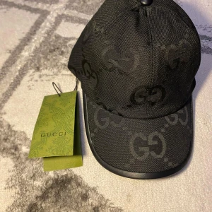 Svart keps från Gucci - Snygg svart keps från Gucci med det ikoniska GG-mönstret. Kepsen har en klassisk design med böjd skärm och justerbart band för perfekt passform. Tillverkad i ett slitstarkt material som ger en lyxig känsla.