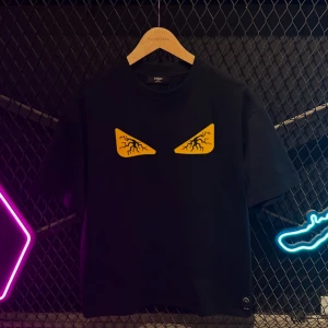 Svart t-shirt med gula ögon från Fendi - Snygg svart t-shirt från Fendi med ett coolt tryck av gula ögon på bröstet. Perfekt för en stilren och edgy look. Kortärmad och i en klassisk passform.