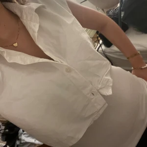 Vit ärmlös skjorta från Monki - Säljer en stilren vit ärmlös skjorta från Monki. Skjortan är croppad och har knappar framtill. Perfekt för en trendig look!