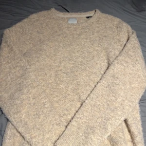 Beige stickad tröja - Mysig beige stickad tröja med långärmad design. Perfekt för kyligare dagar med sin mjuka och bekväma känsla. En stilren och enkel tröja som passar till det mesta.