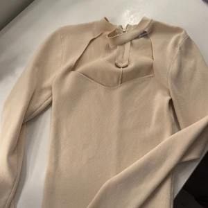 Beige långärmad topp från Zara - Snygg beige långärmad topp från Zara med unik halsdesign och dragkedja i nacken. Perfekt för en stilren look.