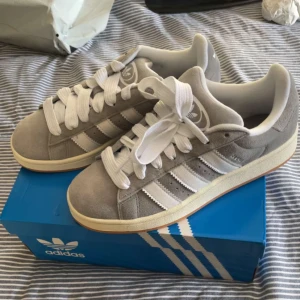 Grå Adidas Campus sneakers - Snygga grå Adidas Campus sneakers i mocka med vita detaljer och snörning. Jätte sköna, men aldrig blivit till användning 