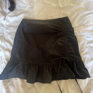 Svart kjol med volang och knyt - Snygg svart kortkjol med volangdetalj och knyt på sidan. 