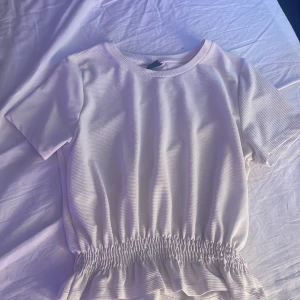 Vit ribbad topp - Säljer en stilren vit ribbad topp med korta ärmar och elastisk midja som ger en fin passform. Perfekt för en avslappnad sommar look!