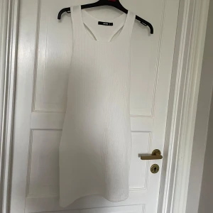 Vit ribbad klänning från bik bok  - Snygg vit ribbad klänning. Den är ärmlös och har en stilren design som passar perfekt för varmare dagar. Klänningen har en tight passform som framhäver figuren.