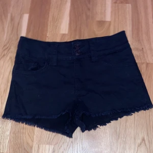 Svarta shorts från H&M - Snygga svarta shorts från H&M med fransiga kanter och två knappar framtill. De har en klassisk femficksdesign. Köpt från barnavdelningen men jag brukar ha storlek XS och dom passar jättebra på mig 